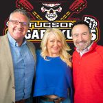 Michael Guymon, Liza Lopez of NOVA Home Loans, and Edmund Marquez pose in front of the Tucson Sugar Skulls logo for The Upside podcast.