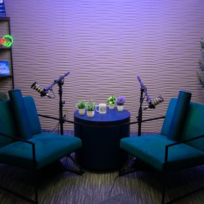 Two teal chairs face a small table, with microphones positioned for recording at Downtown Tucson Podcast Studio.